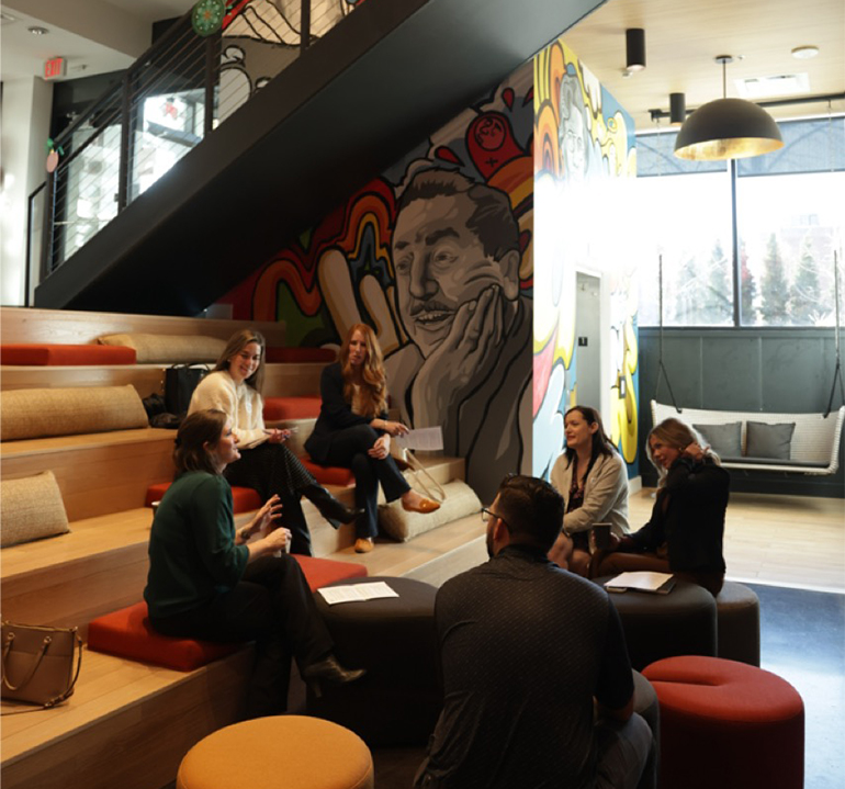 Group of HR leaders conversing in a communal room with a mural of a man behind them