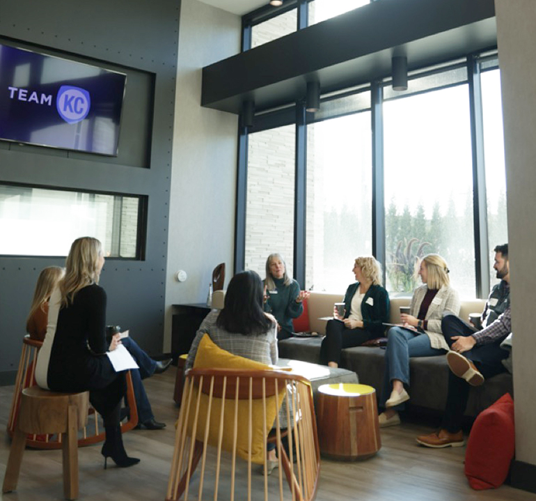 Group of HR leaders conversing in a communal room with a TV displaying TeamKC